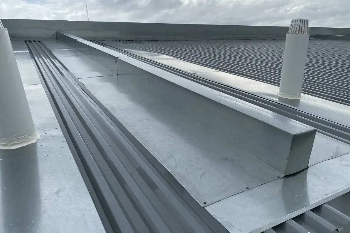 Galvanised box gutter and flashings between corrugated metal roof sheets on a commercial building