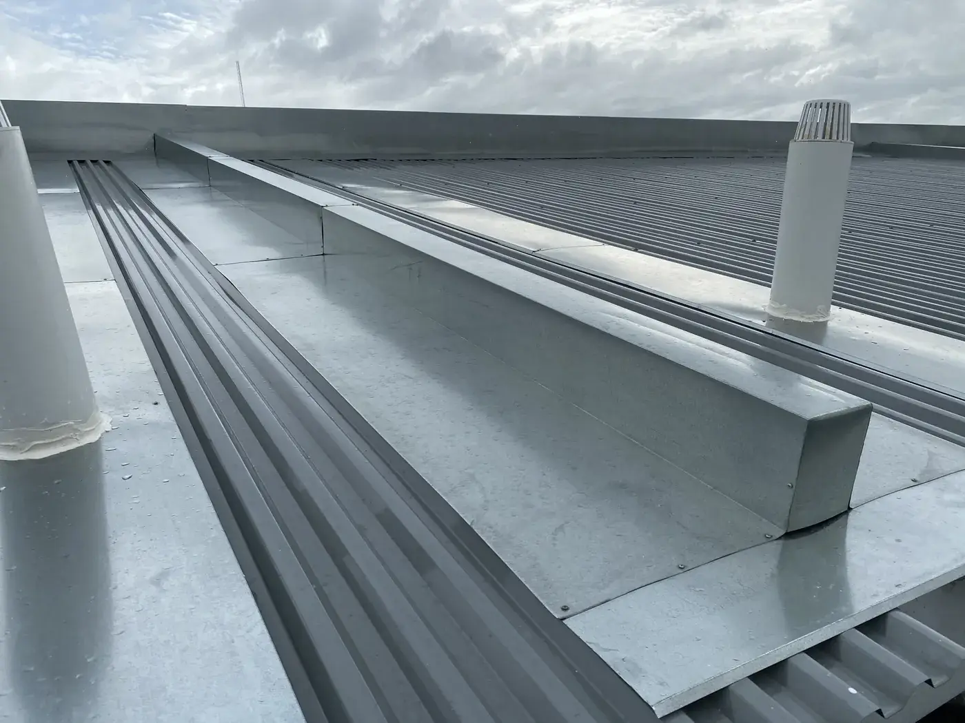 Galvanised box gutter and flashings between corrugated metal roof sheets on a commercial building
