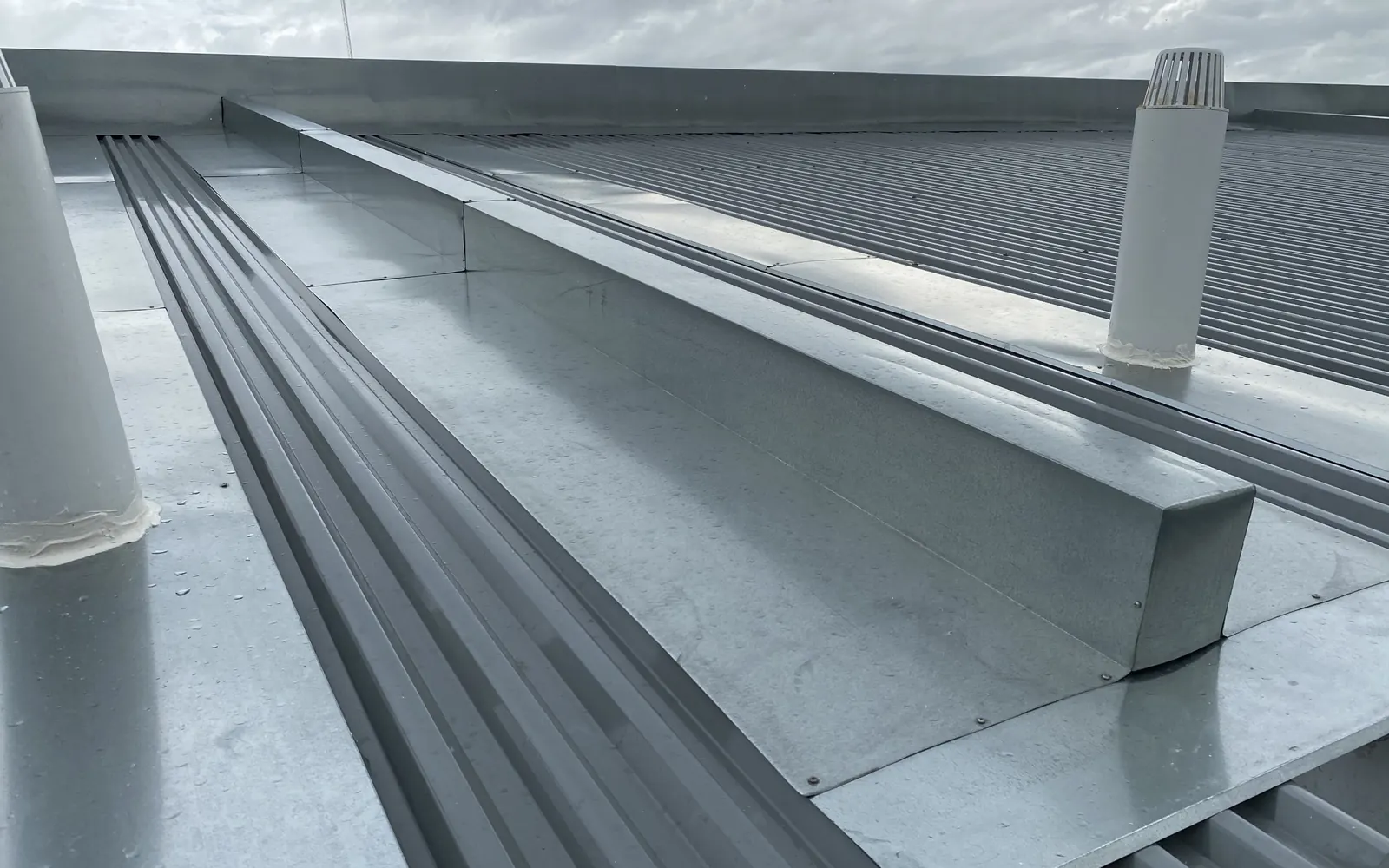 Galvanised box gutter and flashings between corrugated metal roof sheets on a commercial building