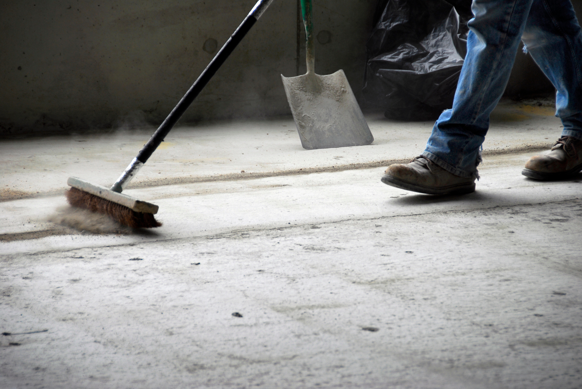 Worker sweeping concrete floor with industrial broom during make good cleaning Melbourne