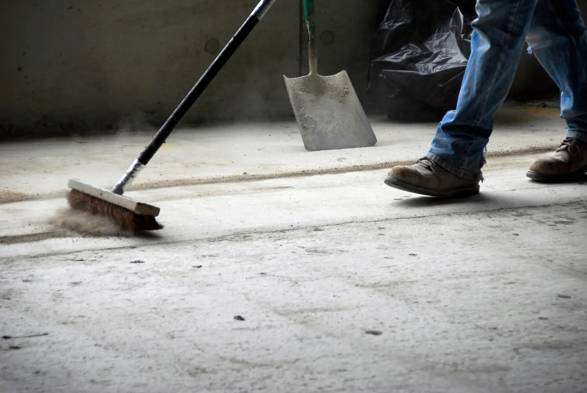 Worker sweeping concrete floor with industrial broom during make good cleaning Melbourne
