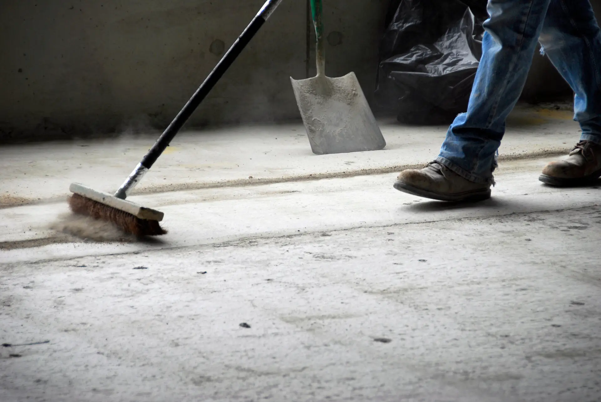 Worker sweeping concrete floor with industrial broom during make good cleaning Melbourne