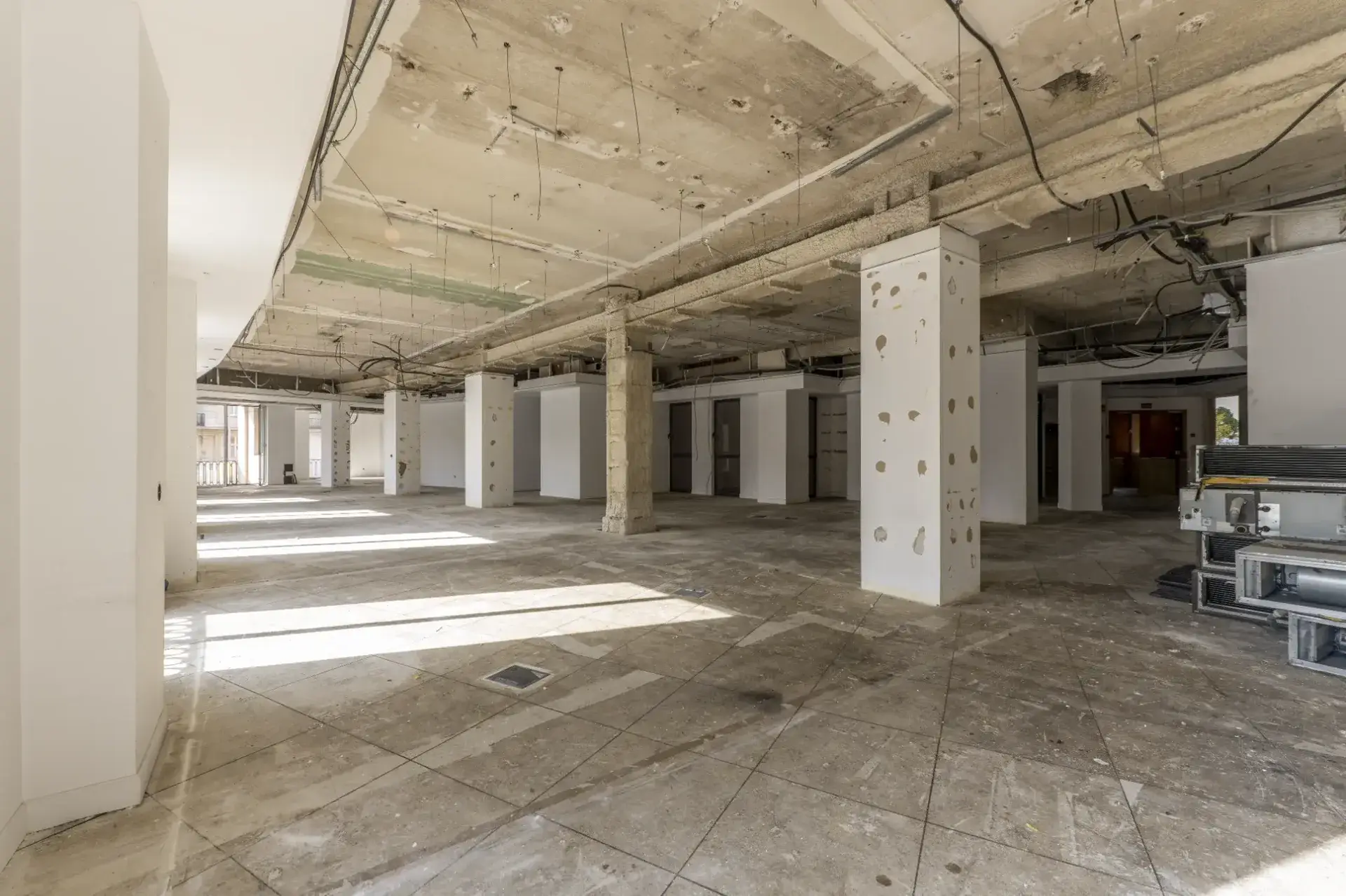 Stripped-out commercial office floor mid-make good in Melbourne showing exposed concrete ceiling, columns with fixing holes and removed partition walls prior to patching and plastering works