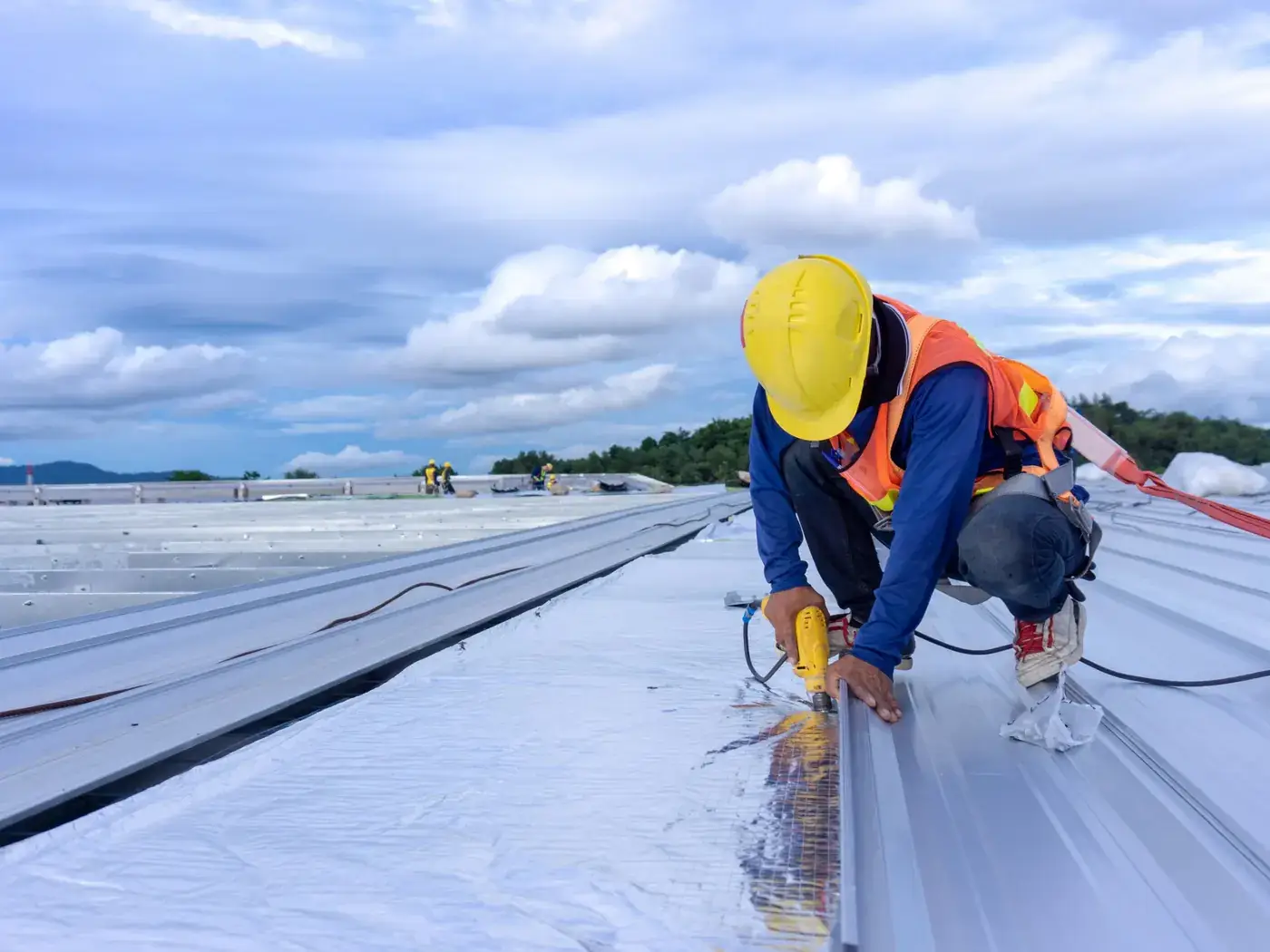 Roofer in a safety harness fixing metal roof sheets on a commercial warehouse