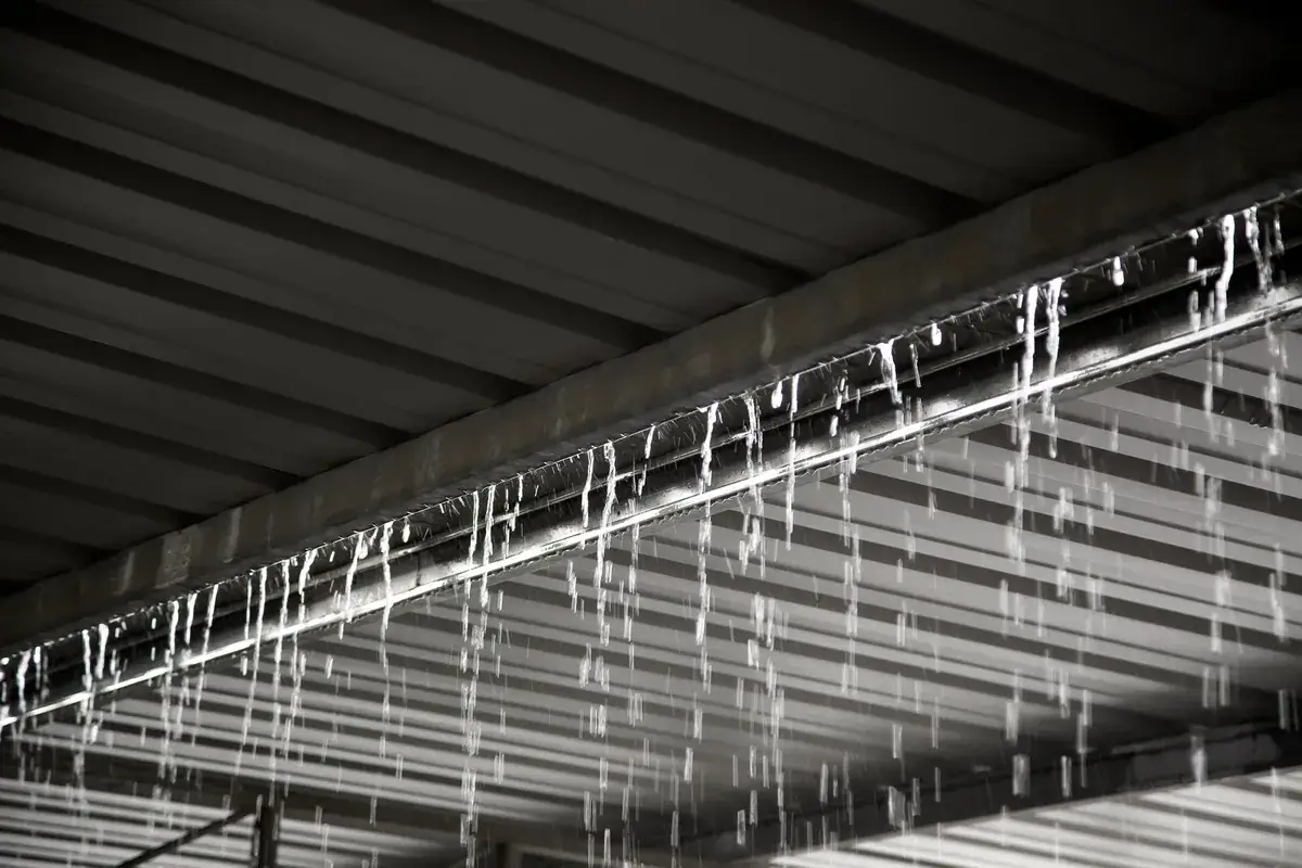 Heavy rain pouring over a gutter beneath a metal warehouse roof during a storm in Melbourne