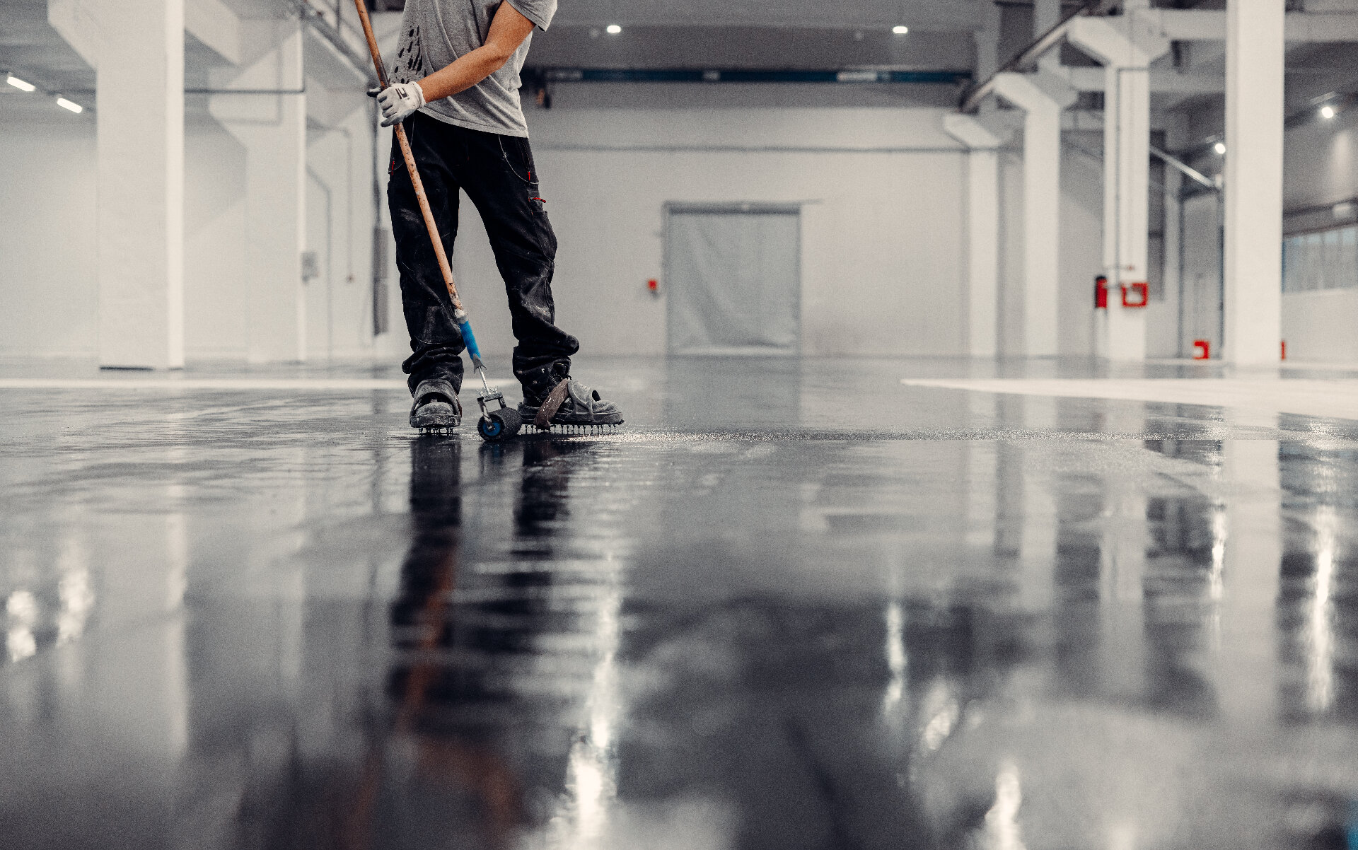 Worker applying protective floor sealant coating to ground concrete warehouse floor Melbourne