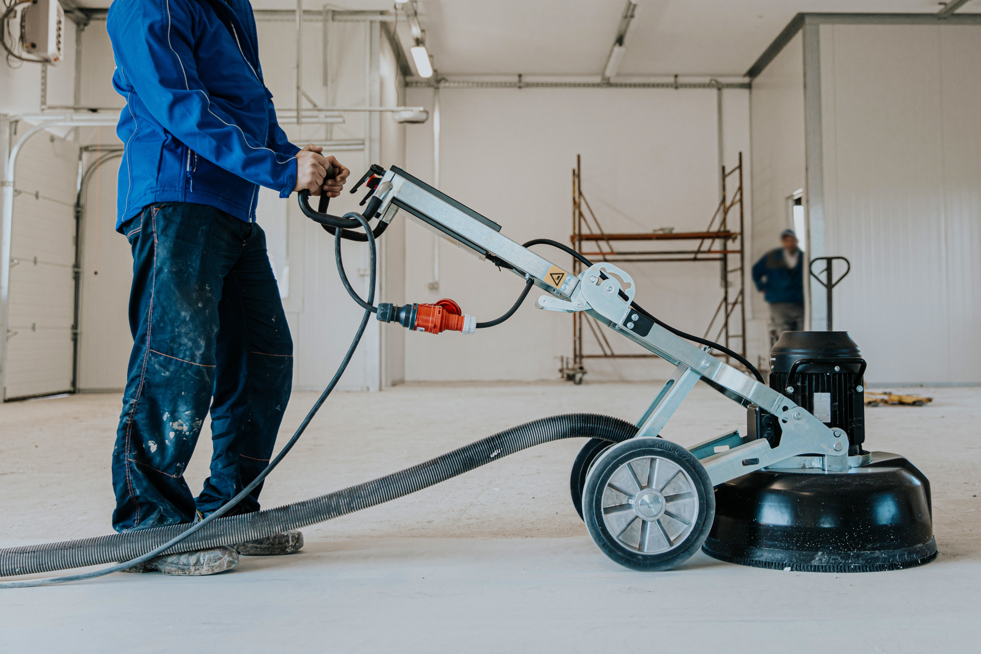 Worker operating industrial concrete floor grinder with vacuum dust extraction in Melbourne warehouse