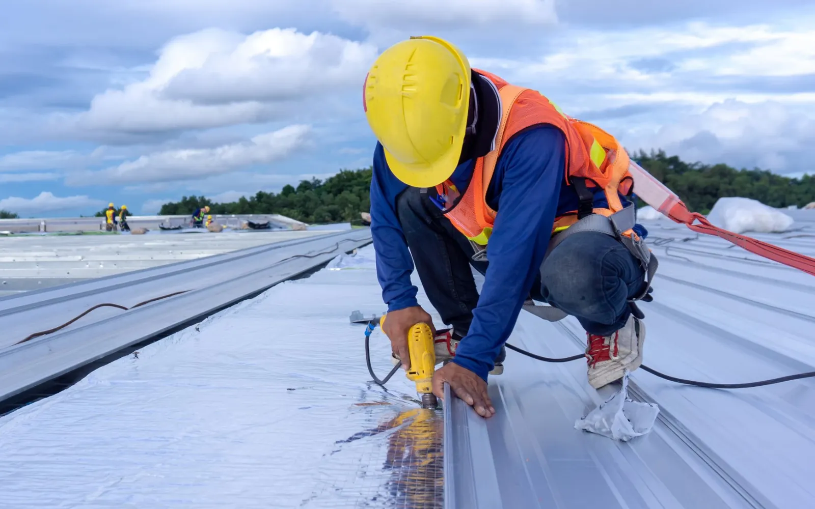 Roofer in a safety harness fixing metal roof sheets on a commercial warehouse