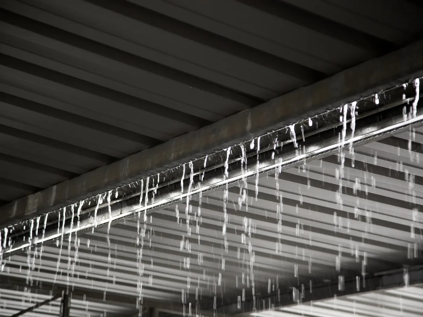 Heavy rain pouring over a gutter beneath a metal warehouse roof during a storm