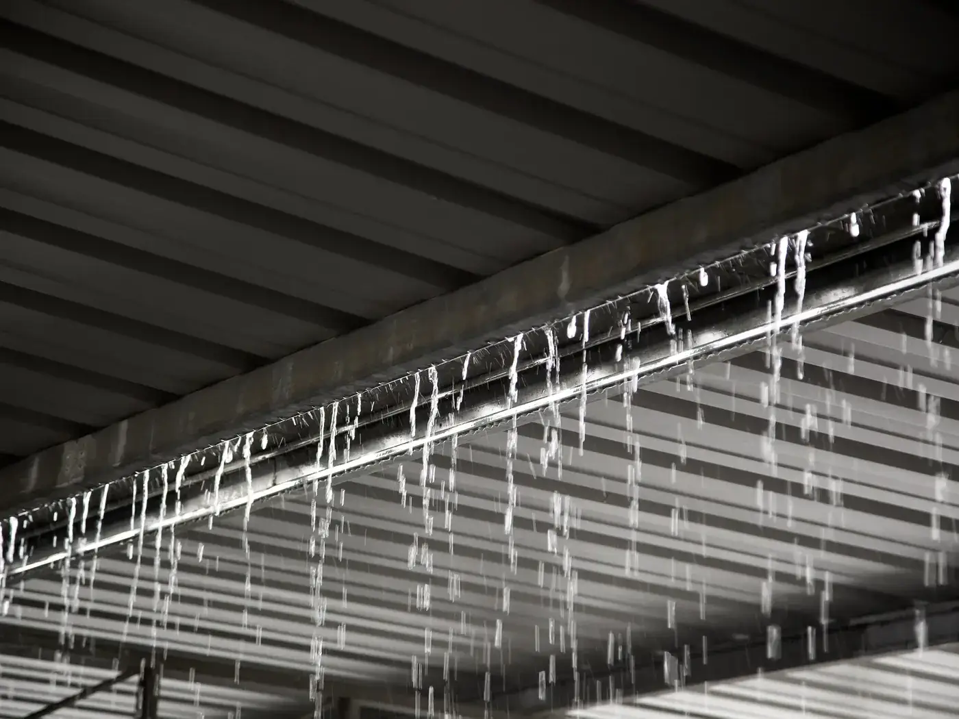 Heavy rain pouring over a gutter beneath a metal warehouse roof during a storm