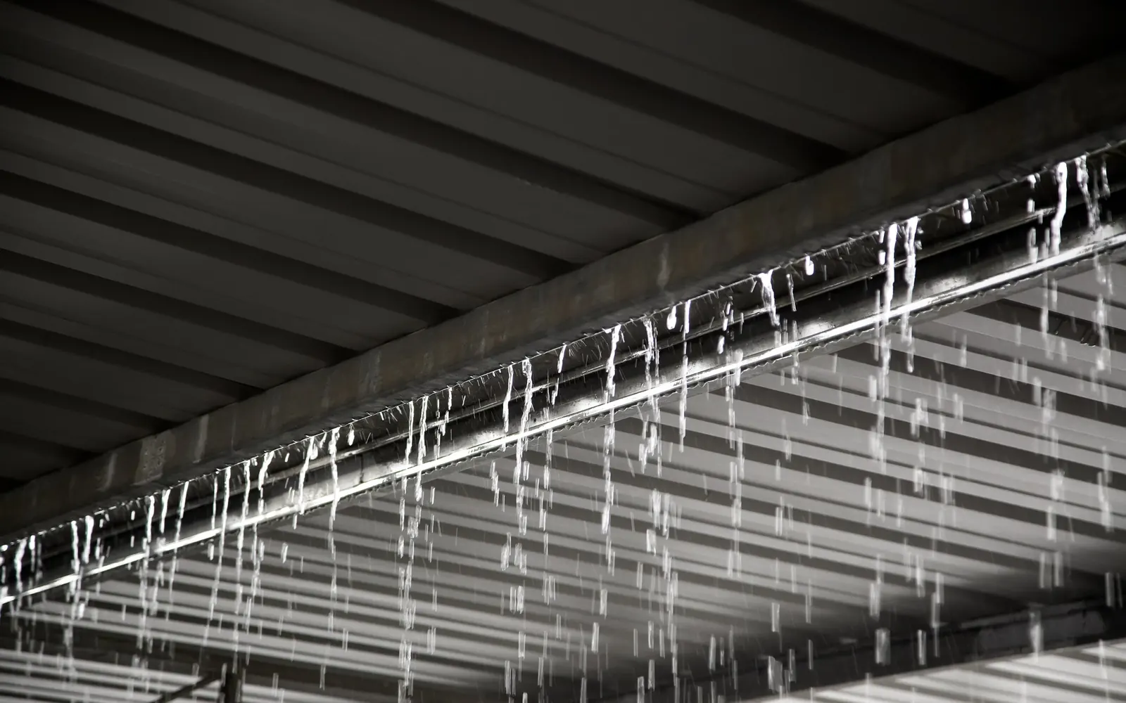 Heavy rain pouring over a gutter beneath a metal warehouse roof during a storm