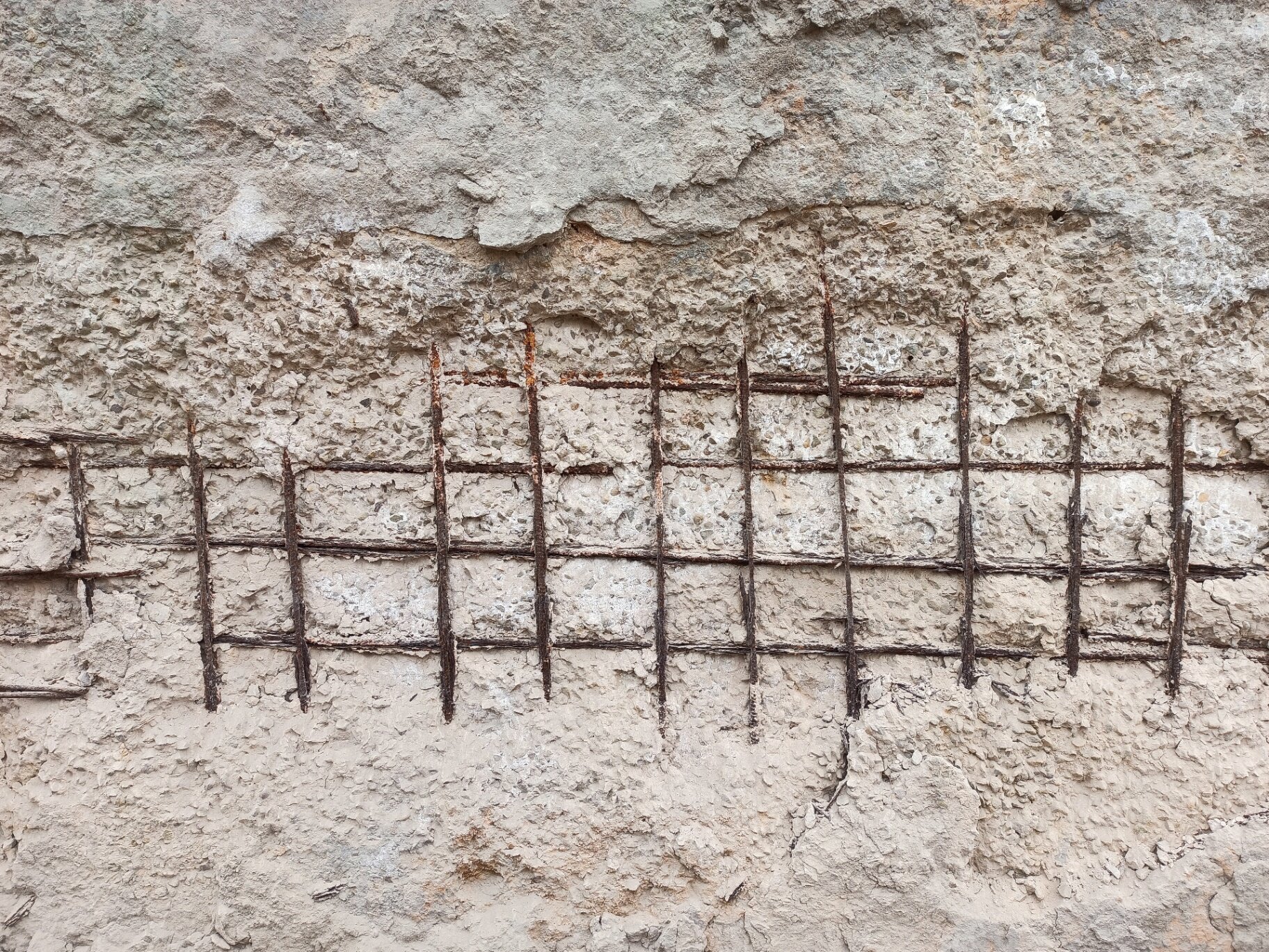 Close-up of exposed and rusted rebar in a damaged concrete wall, showing a severe case of concrete cancer requiring structural remediation