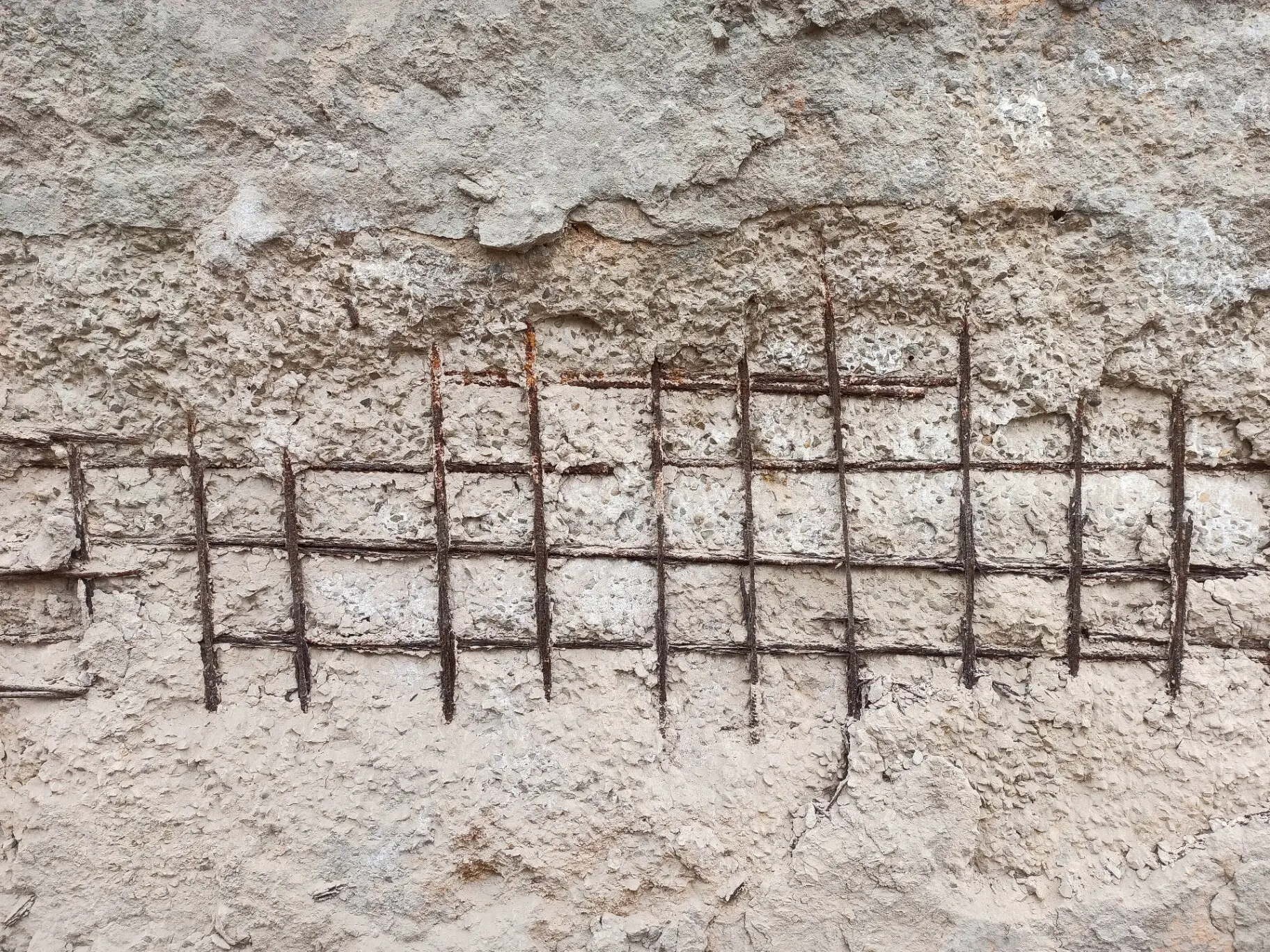 Close-up of exposed and rusted rebar in a damaged concrete wall, showing a severe case of concrete cancer requiring structural remediation