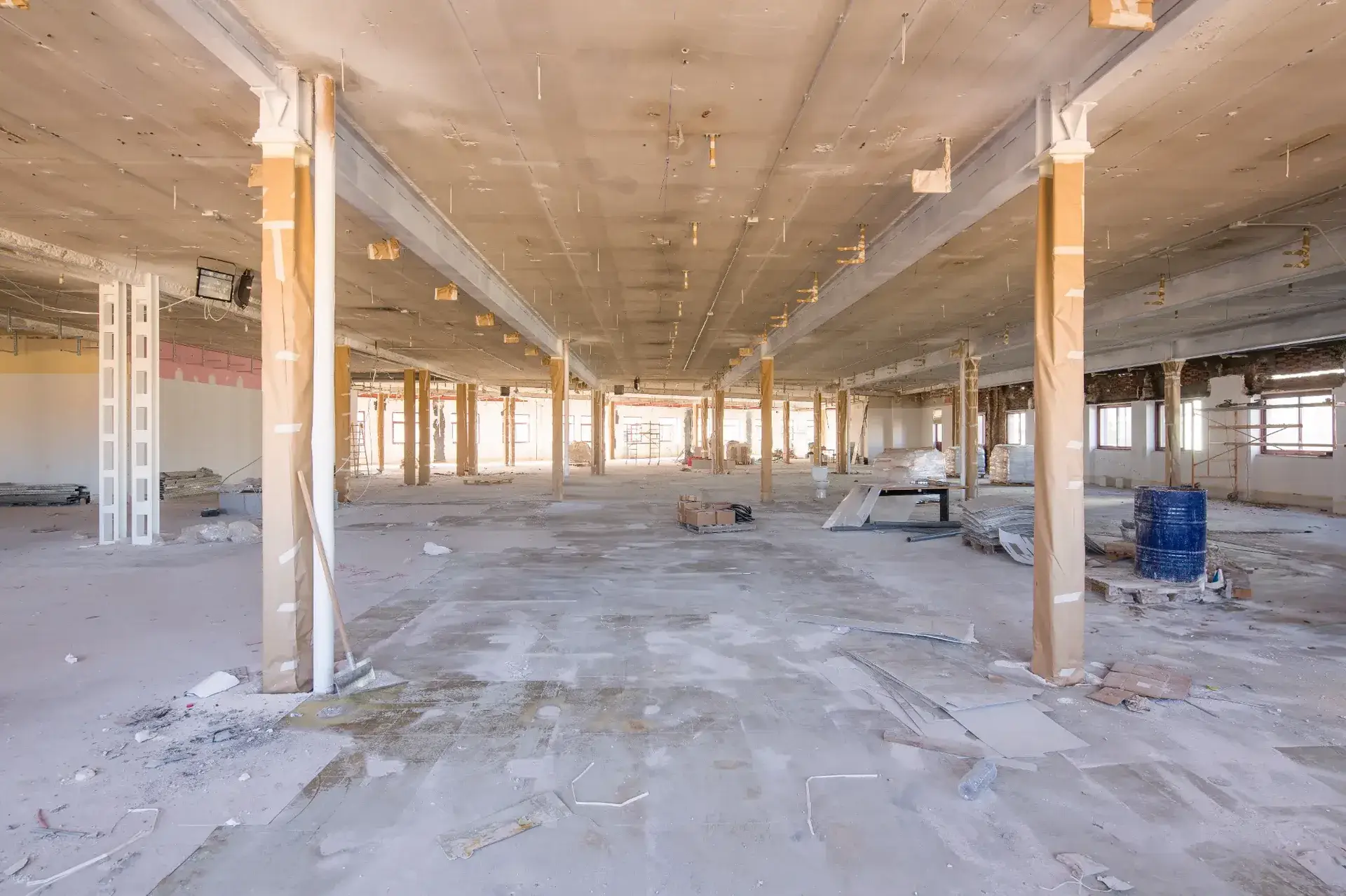Large commercial warehouse interior mid-demolition with exposed concrete slab, steel columns and construction debris during strip out works in Melbourne